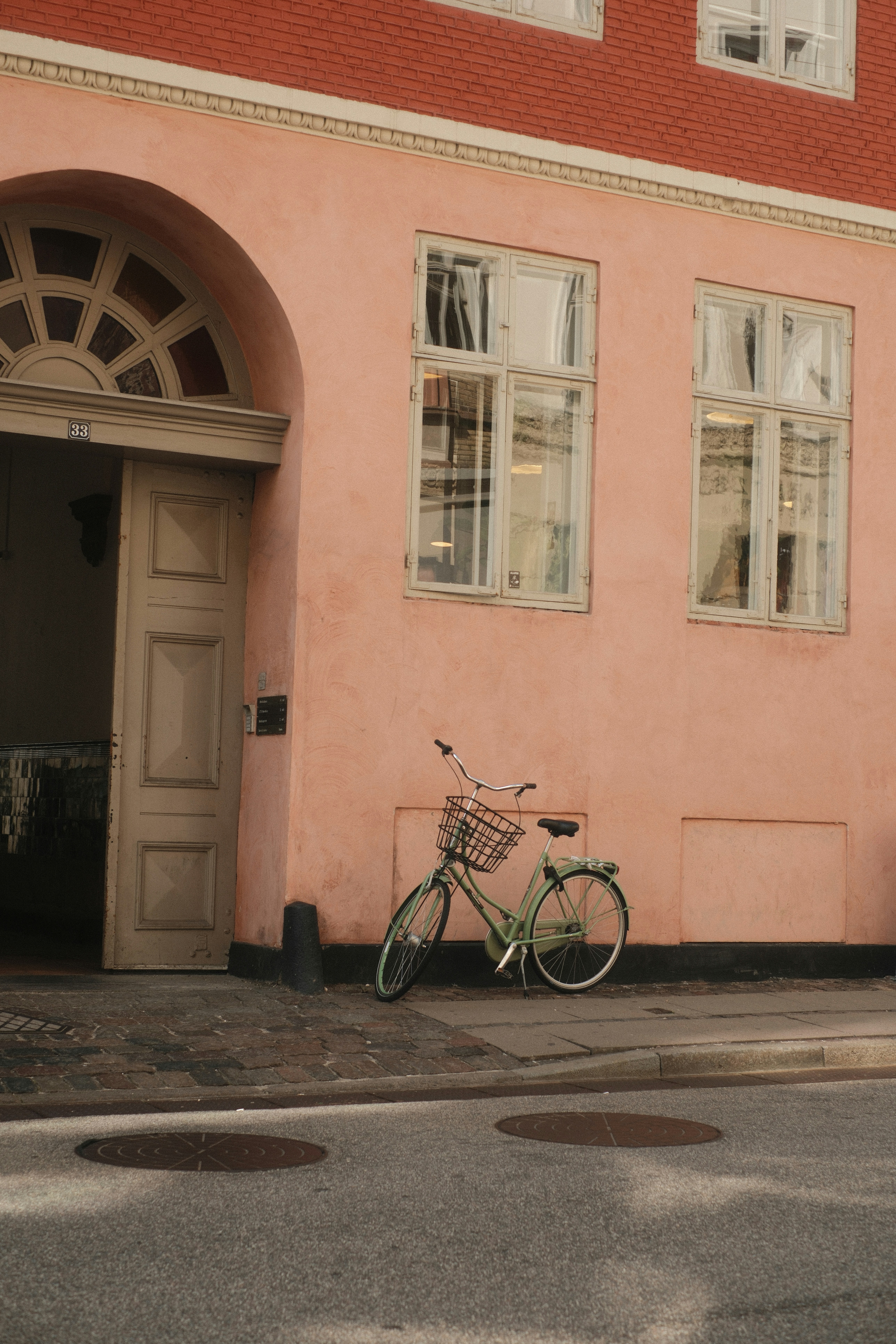 A bicycle rests against a pastel pink building.