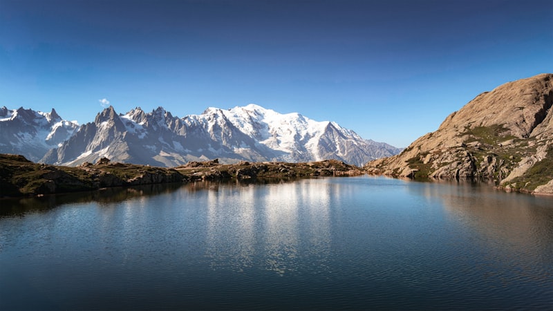 Snow-streaked Mont Blanc massif reflected in a perfectly still alpine lake under a deep blue sky