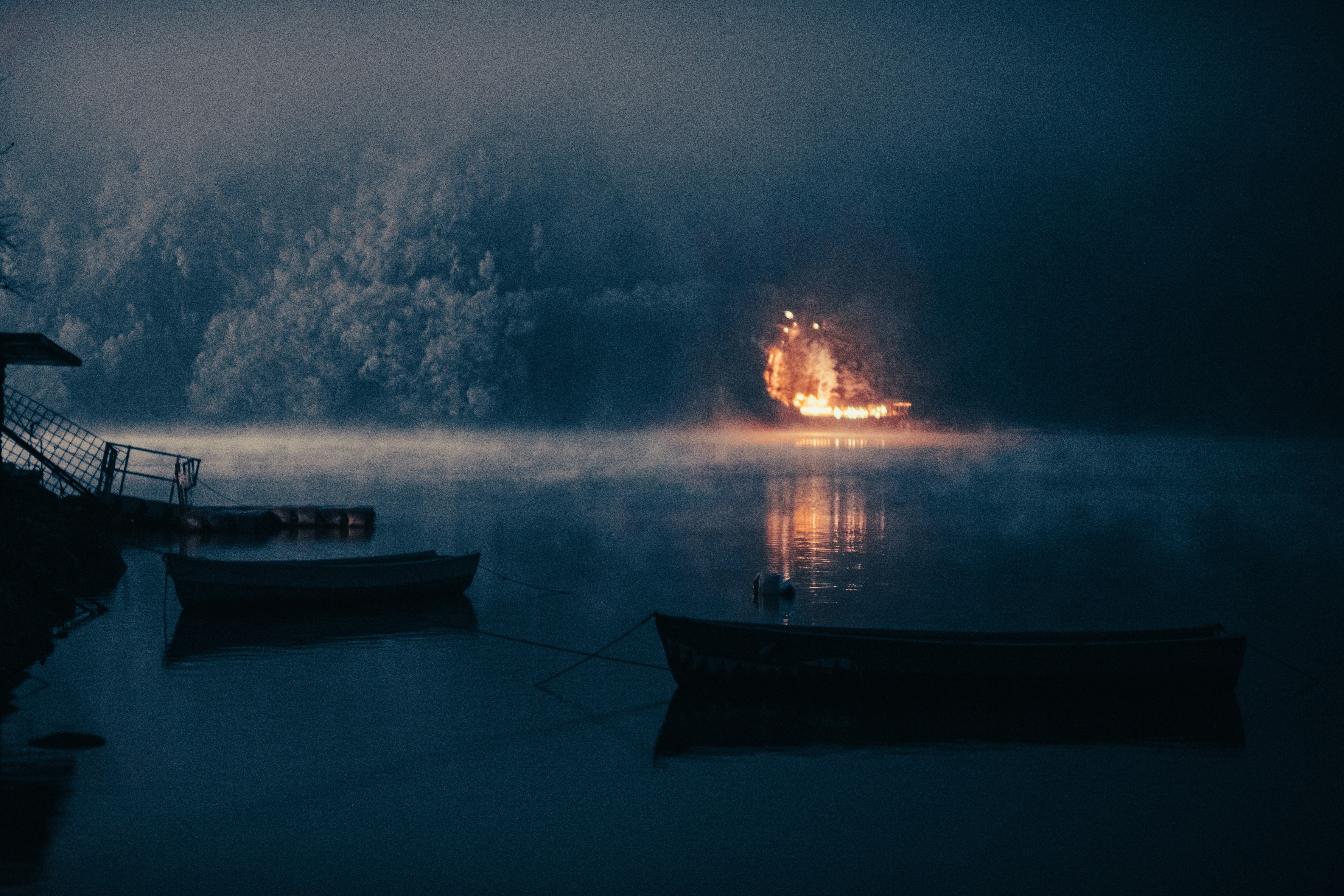 Fire burns on water in a misty, dark scene.