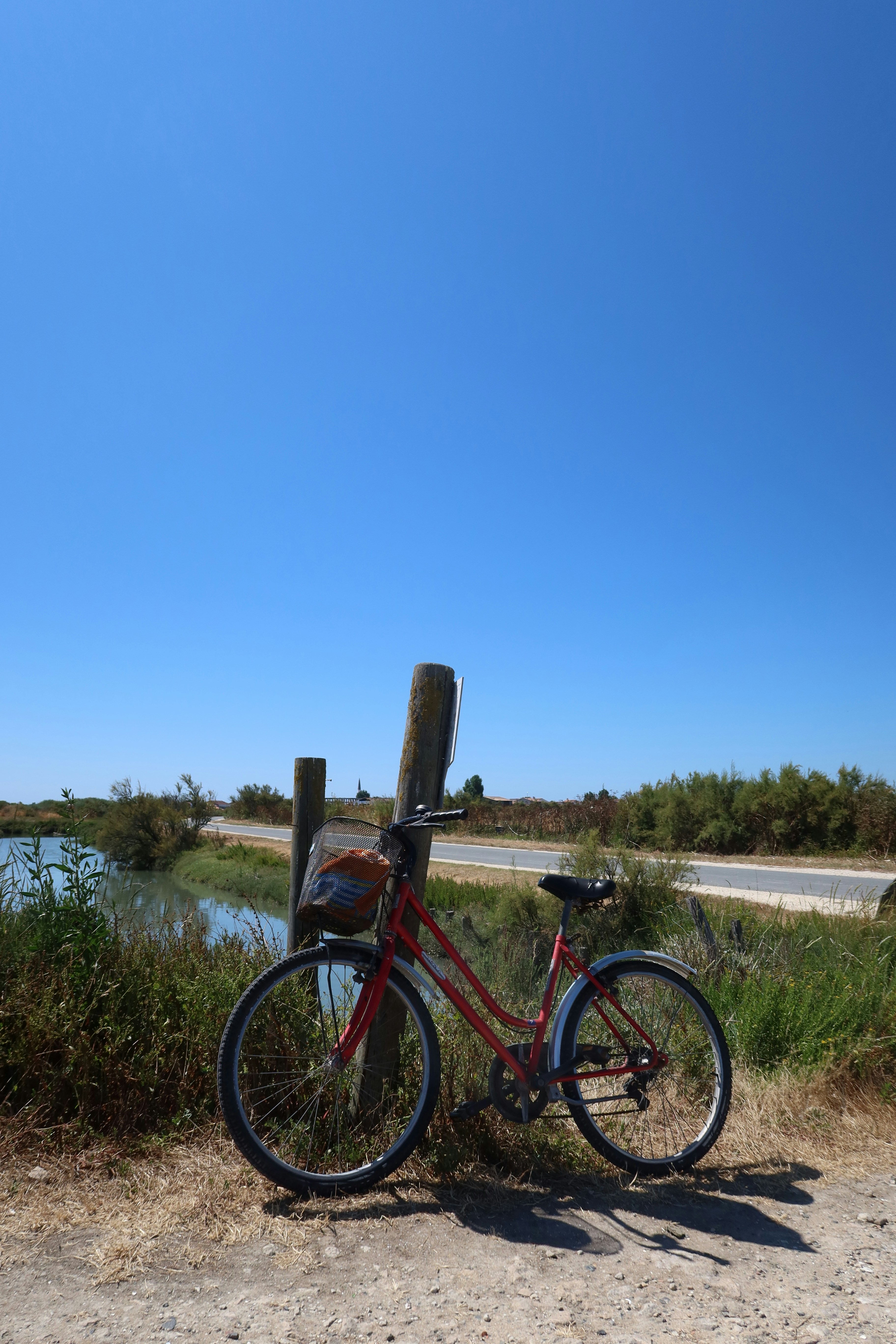 A red bicycle rests by water and clear skies.