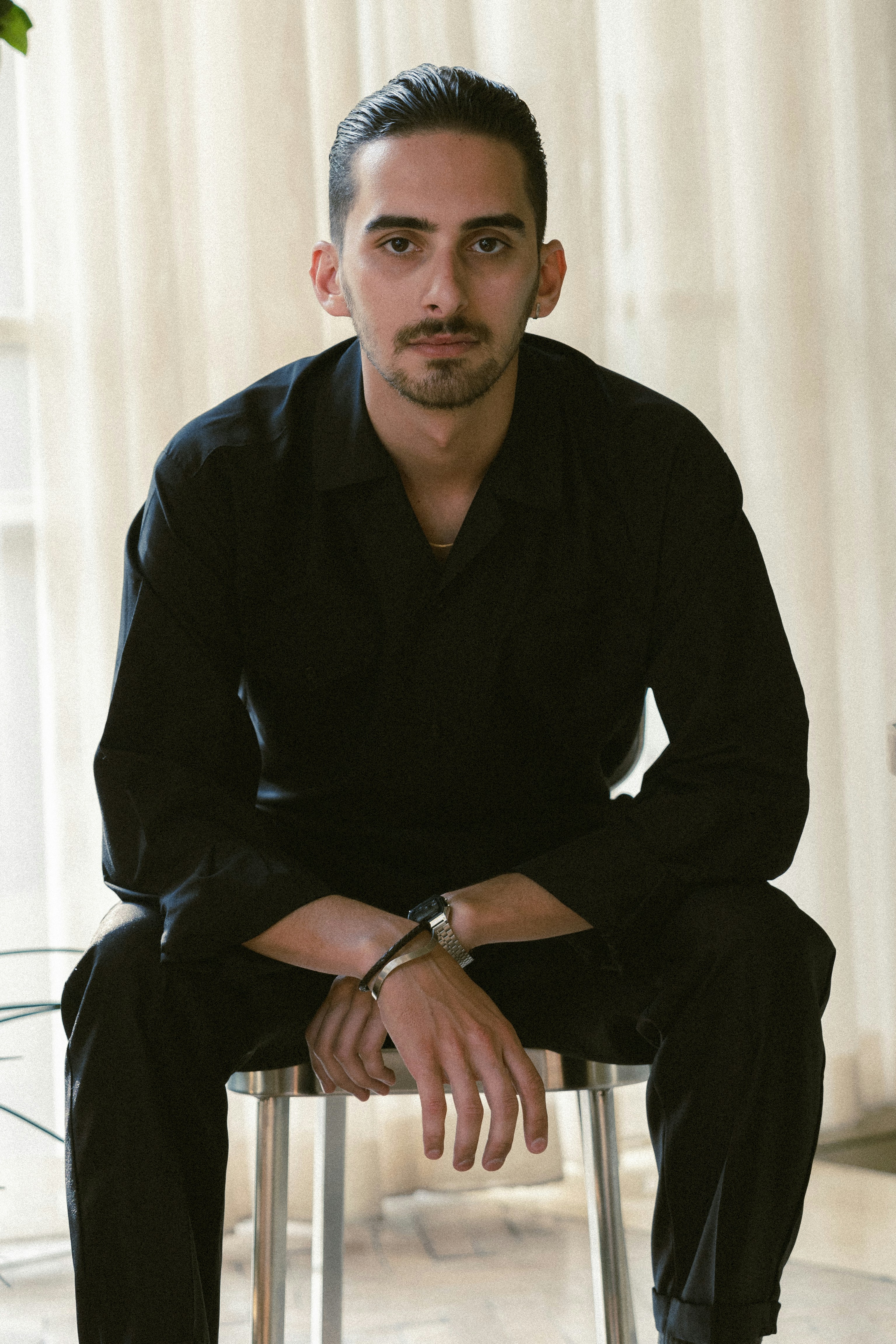 Man sits in a chair, wearing black clothing.