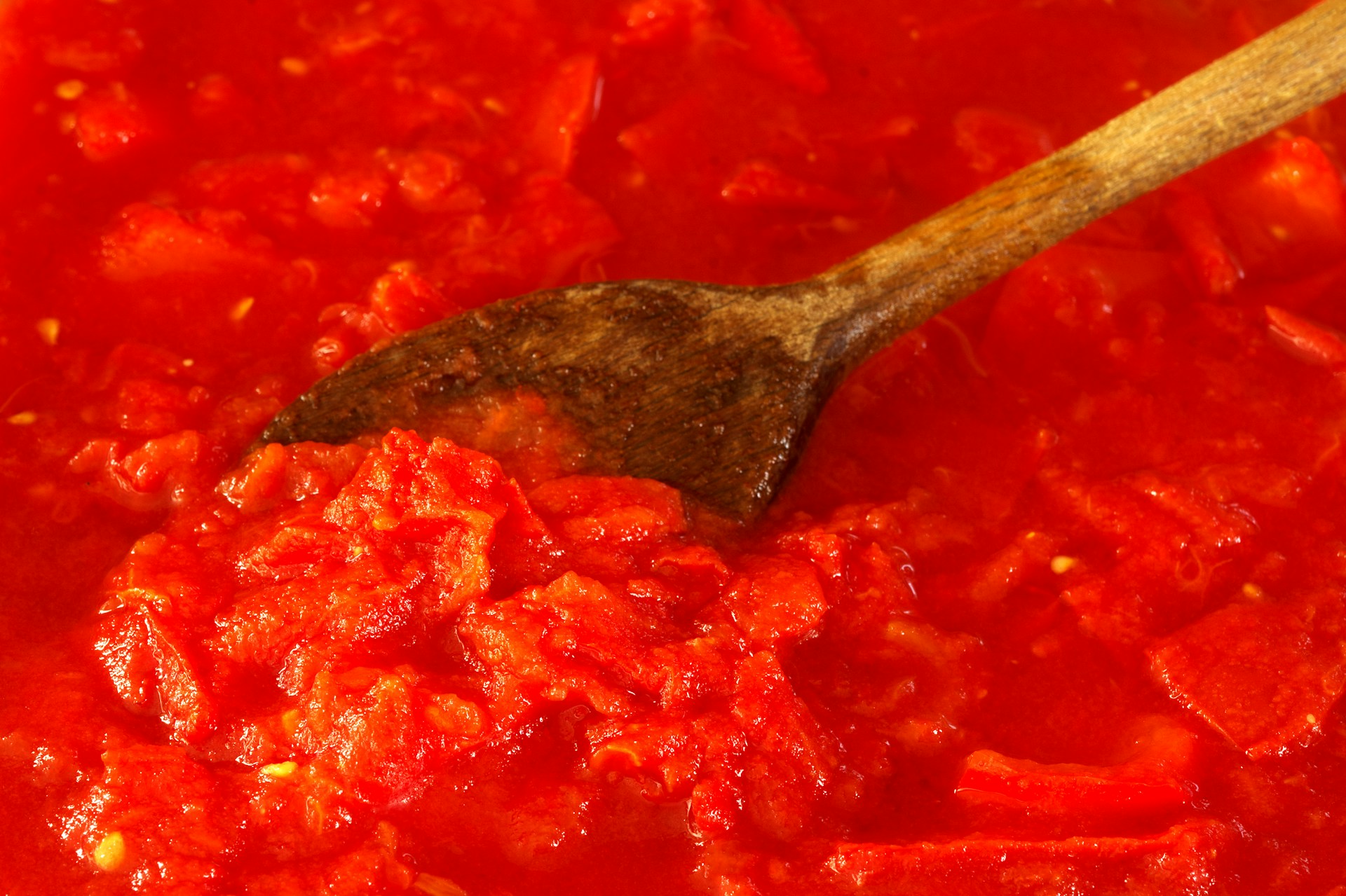 Tomato sauce being stirred with a wooden spoon.