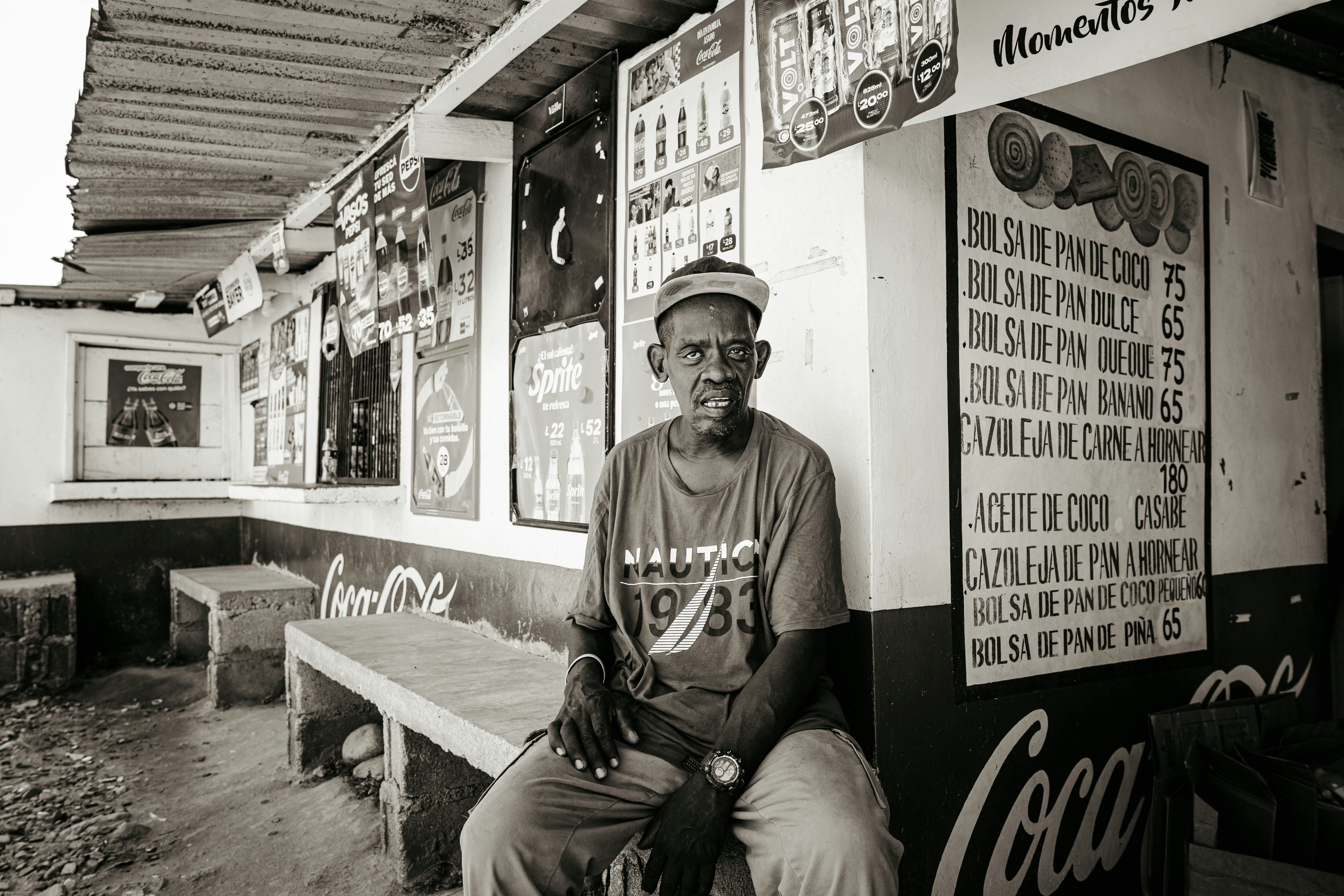 A man sits outside a small store.