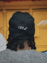 A person with locs wearing a black hat.