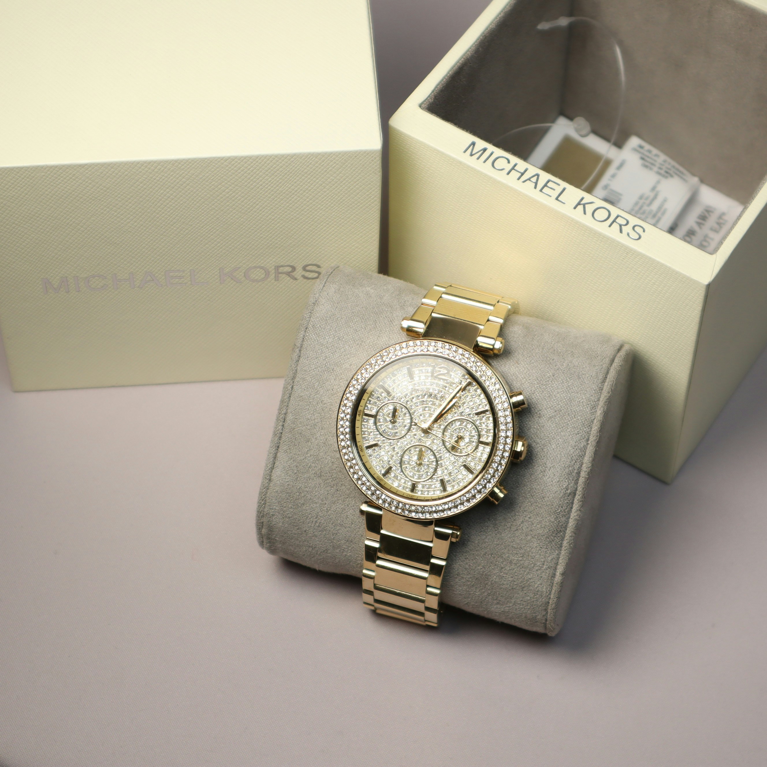 A gold michael kors watch sits near its box.