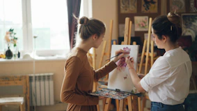 Two women paint together in a bright art studio.