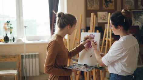 Two women paint together in a bright art studio.