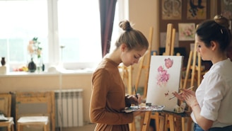 Two women paint together in a bright art studio.