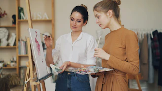 Two women are painting and discussing art.