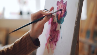 A hand paints a flower on canvas.