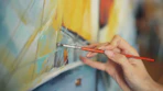 An artist's hand paints on a canvas.