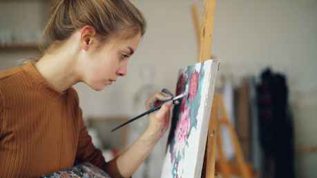 A young woman is painting a floral artwork.