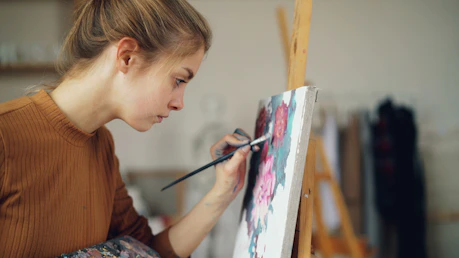 A young woman is painting a floral artwork.