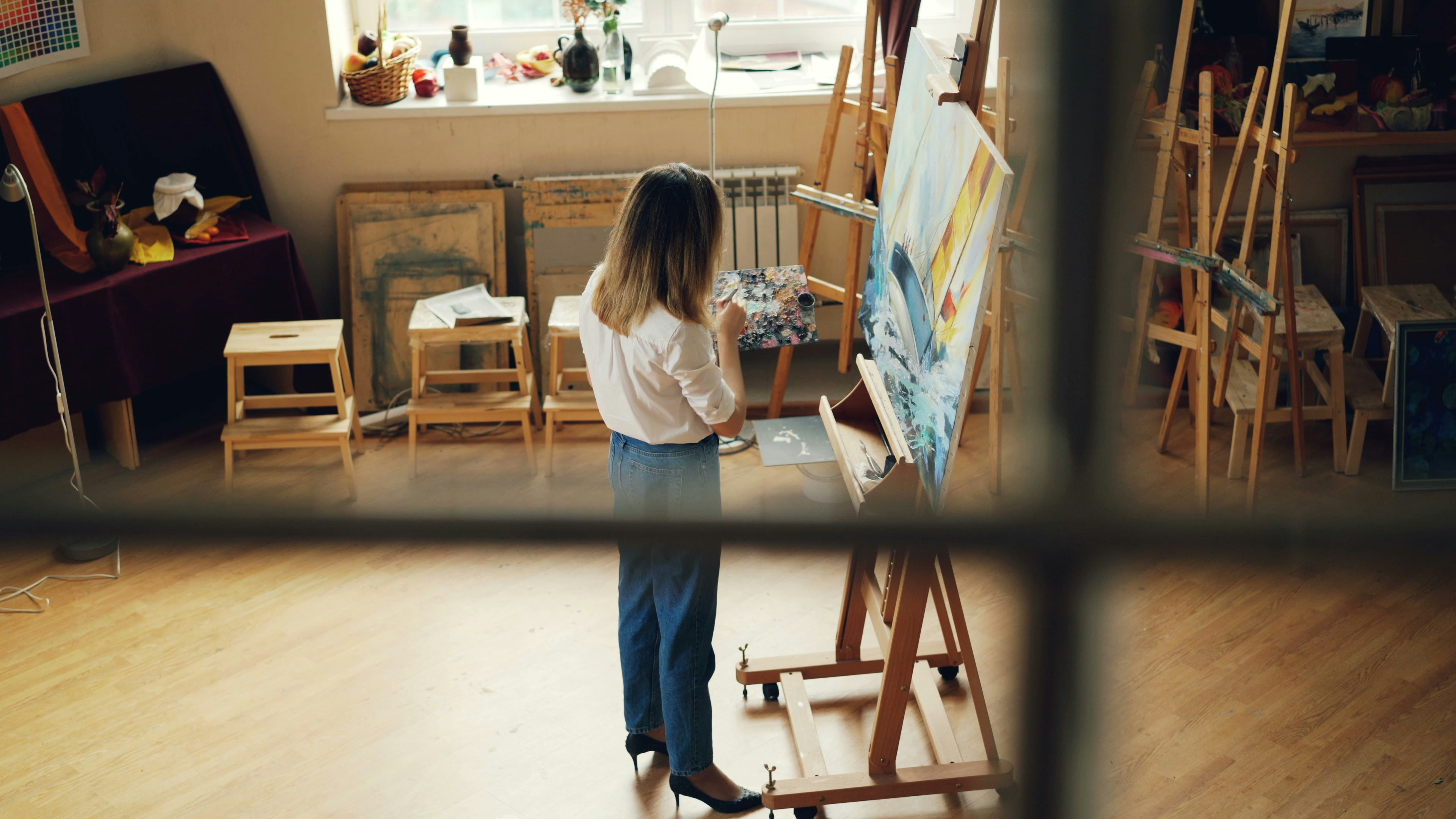 A woman paints in her sunny art studio.