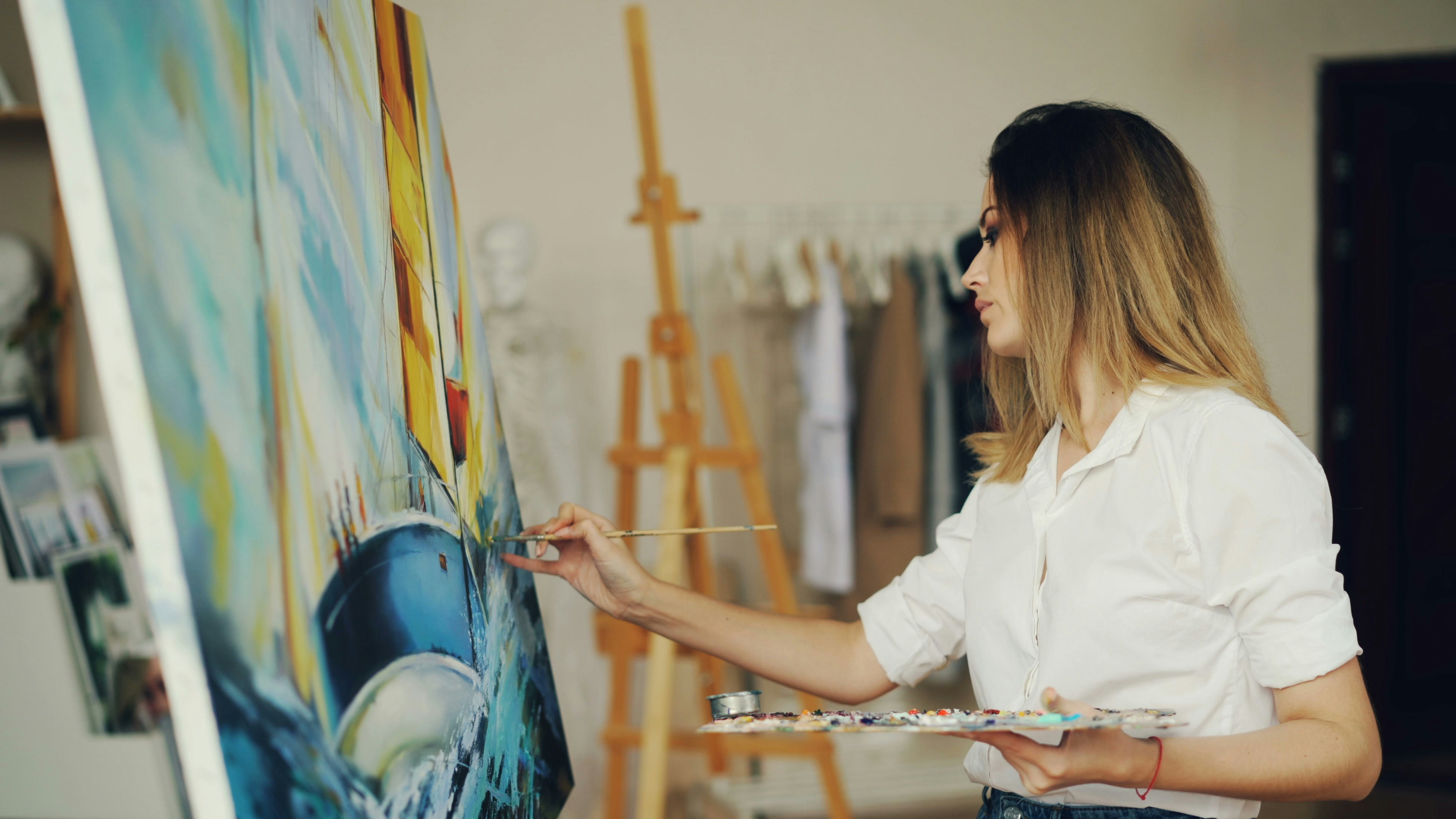 Artist paints on canvas in a light-filled studio.