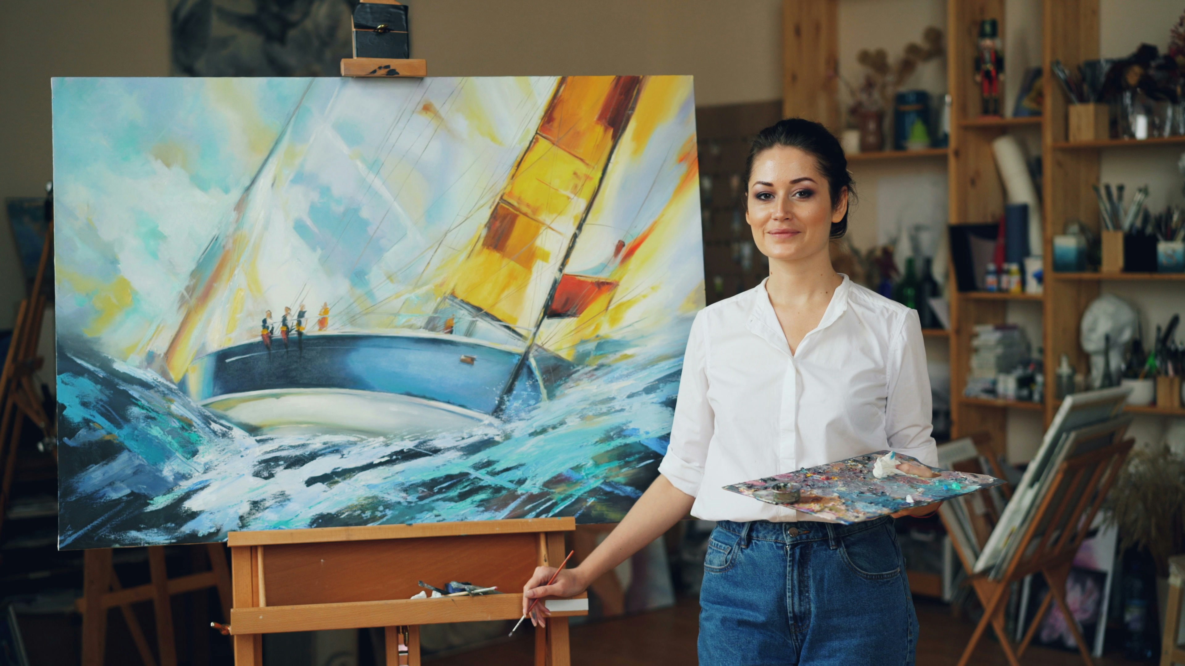 A woman stands by her painting of a sailboat.