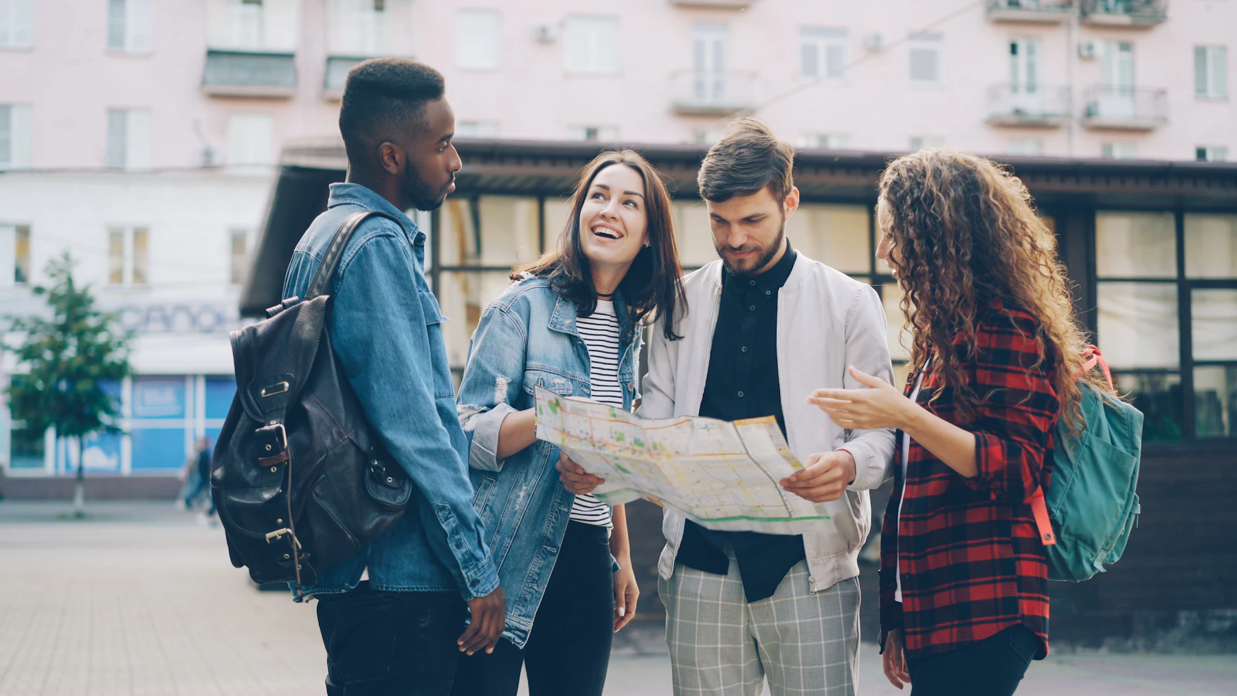 Four friends with backpacks reading a paper map together on a city square