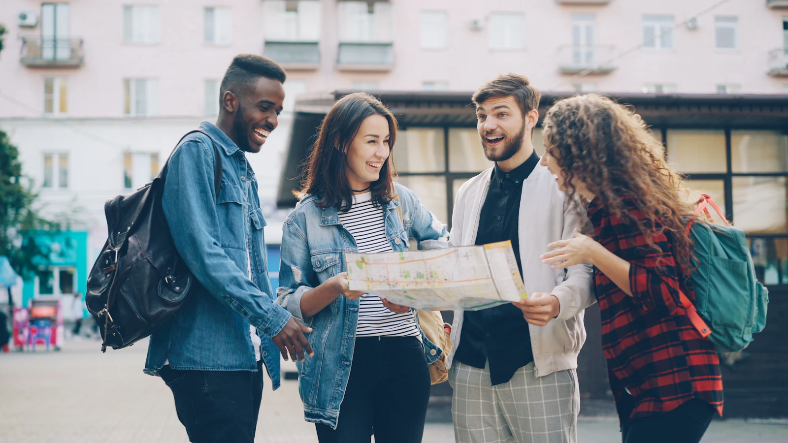 Grupo de amigos estudantes com mochilas sorrindo e olhando um mapa numa rua da cidade