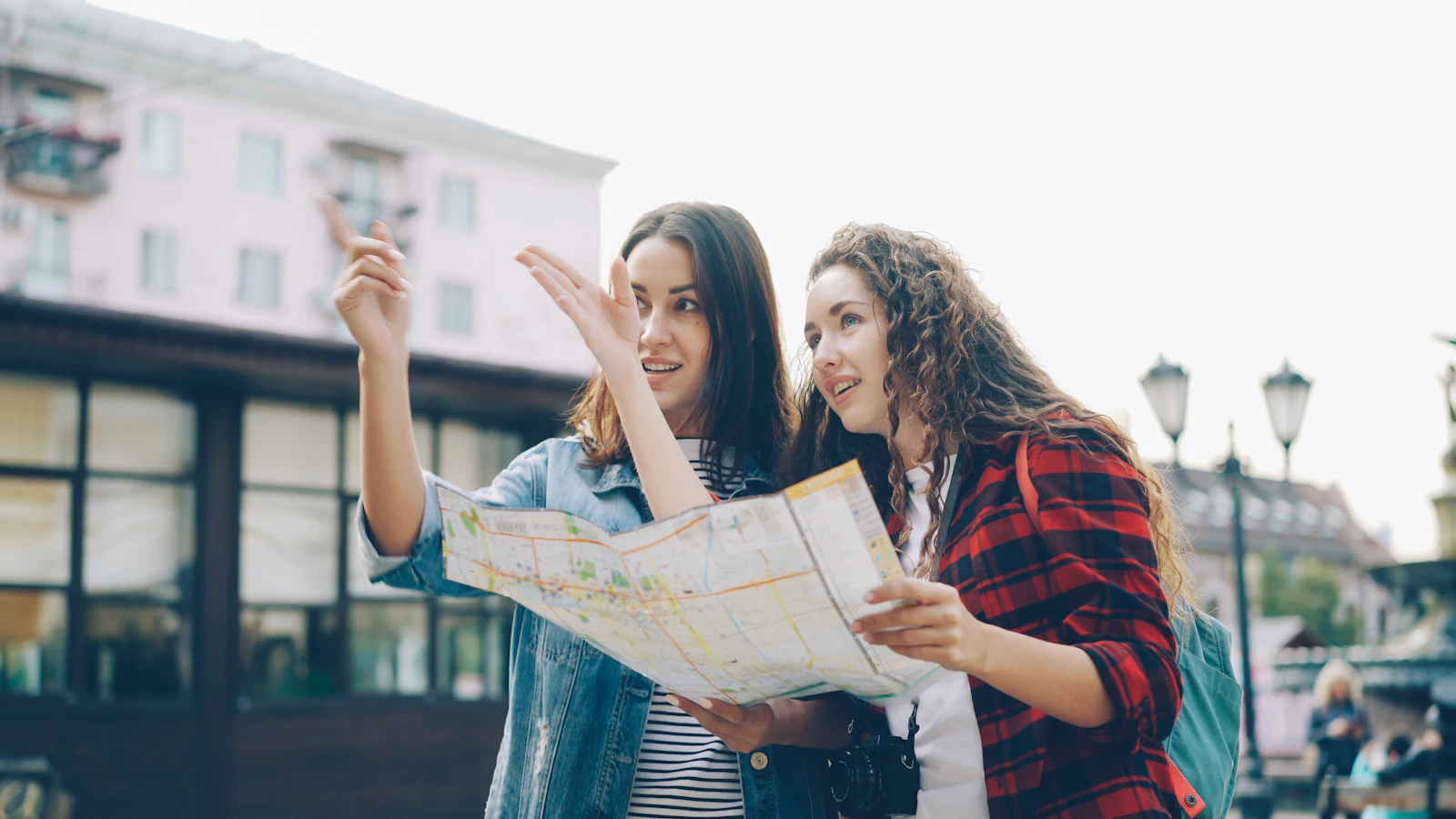 Duas jovens viajantes conversando e consultando um mapa numa rua de cidade europeia