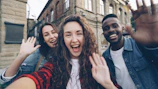 Friends wave excitedly, taking a selfie together.