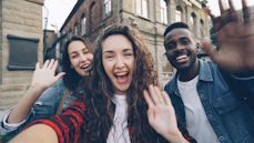 Friends wave excitedly, taking a selfie together.