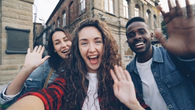 Friends wave excitedly, taking a selfie together.