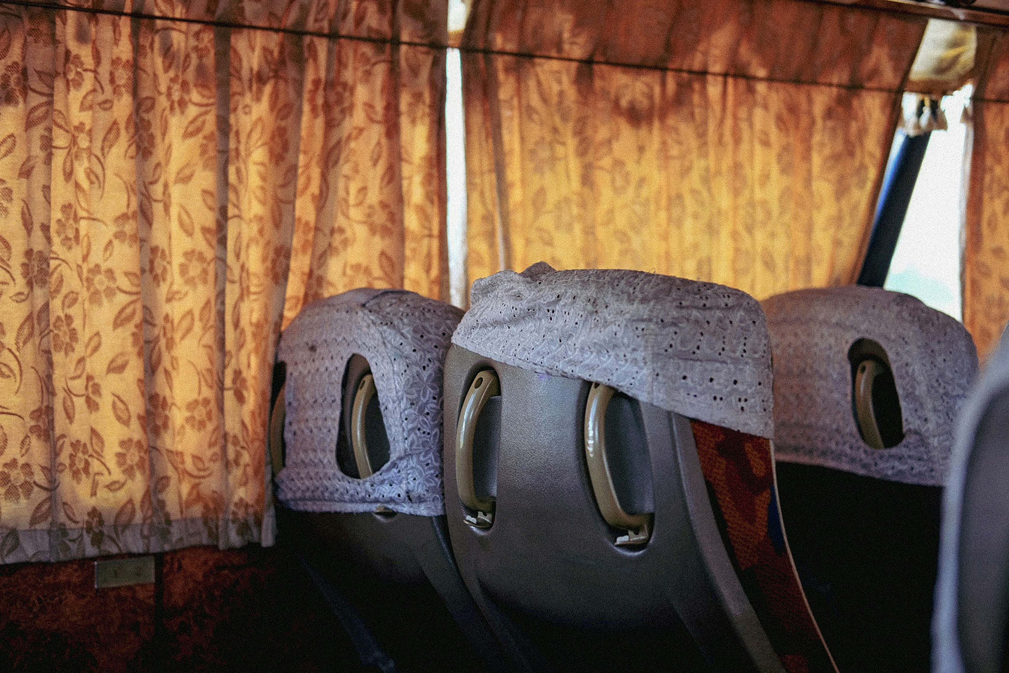 Inside of a bus with seatbacks and curtains.