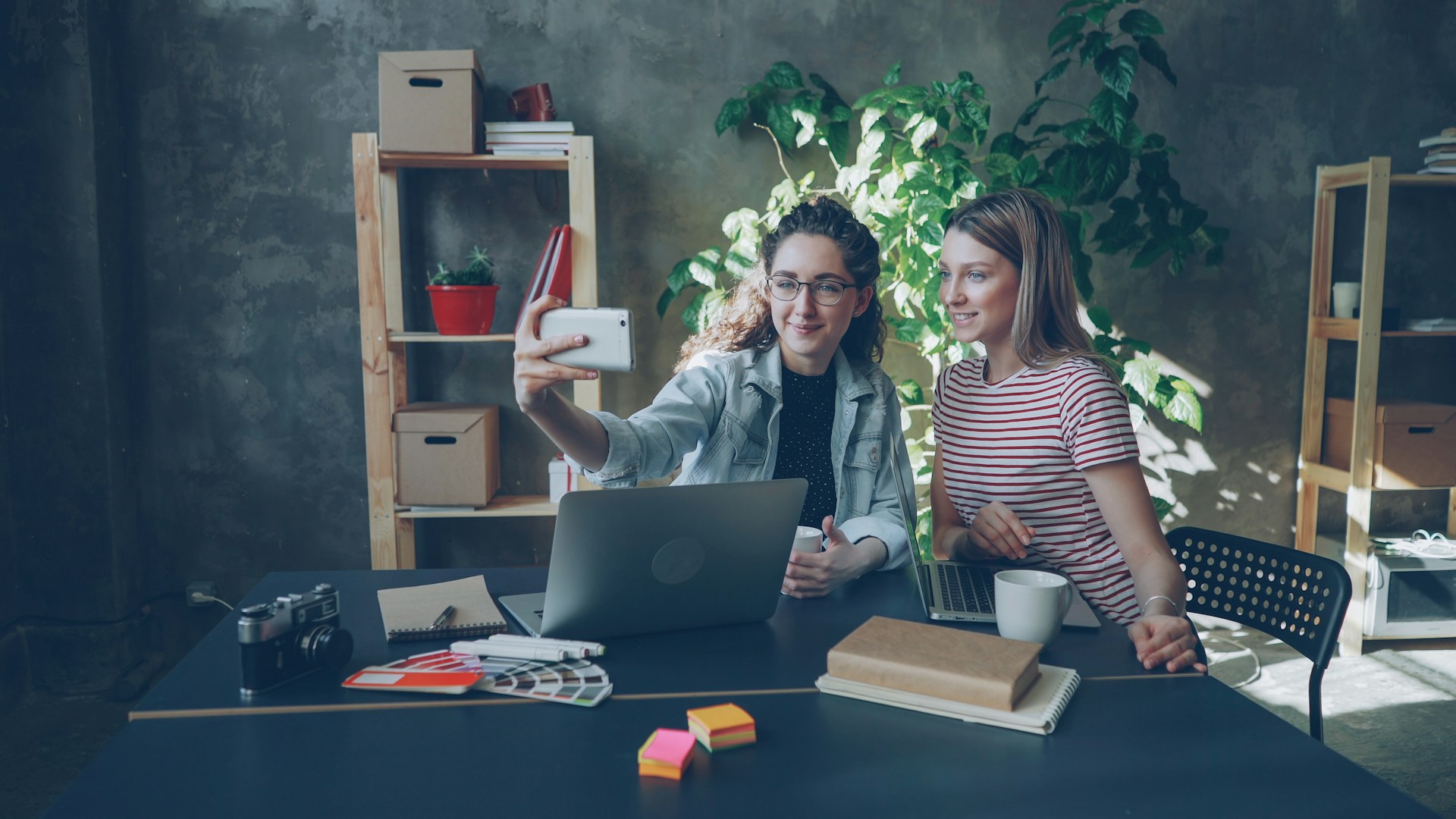 Two women take a selfie at a desk.