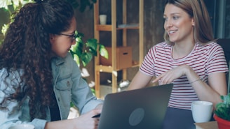 Two women work together on a laptop.