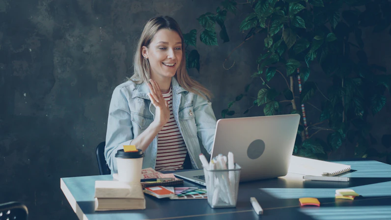 Woman waving during a video call on her laptop.