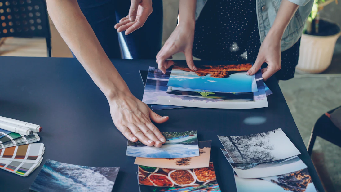 Hands arranging photographs and colors across a worktable