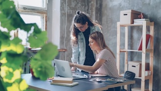 Two women collaborate at a laptop in an office.