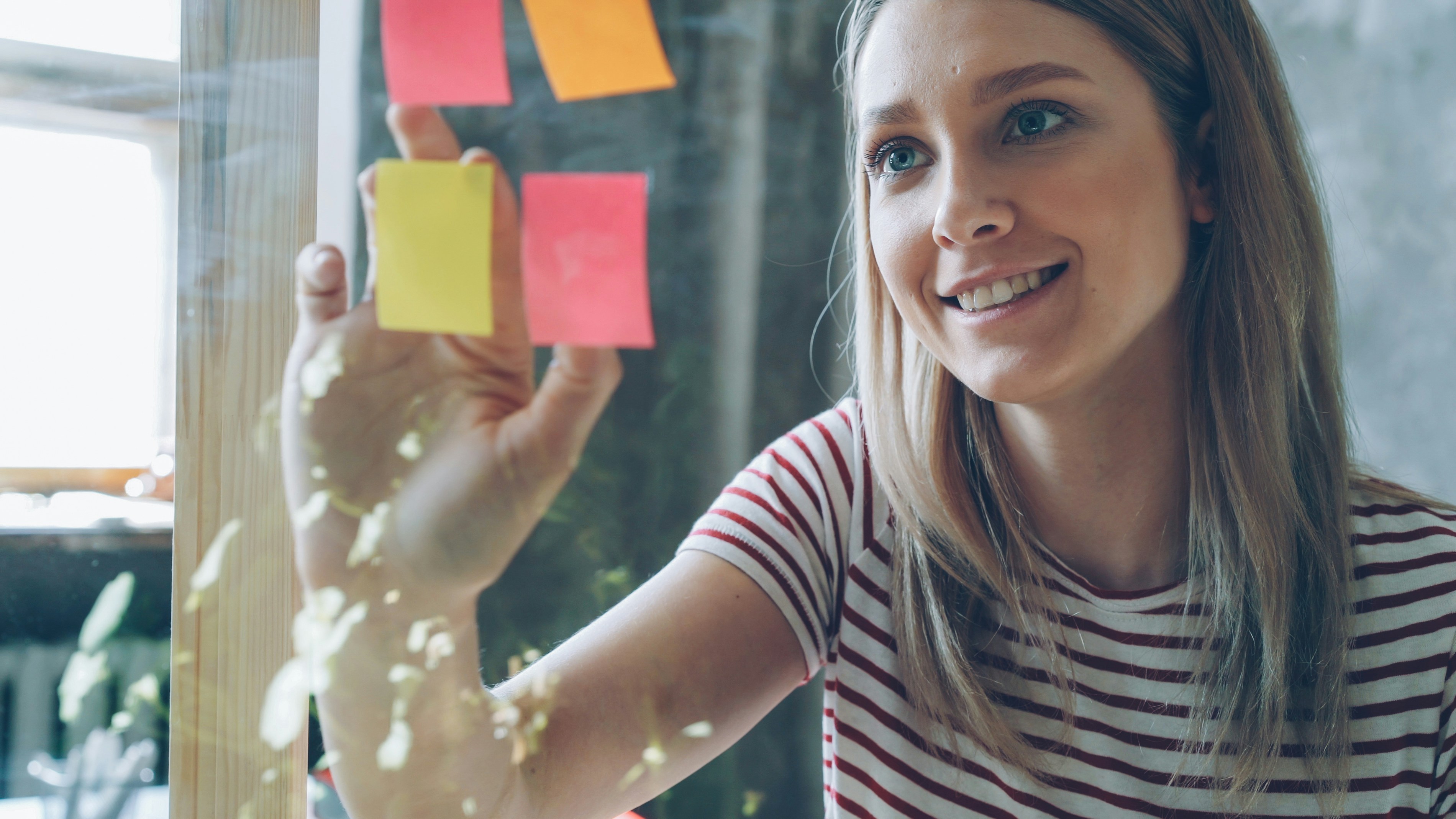 Woman posts sticky notes on a glass surface.