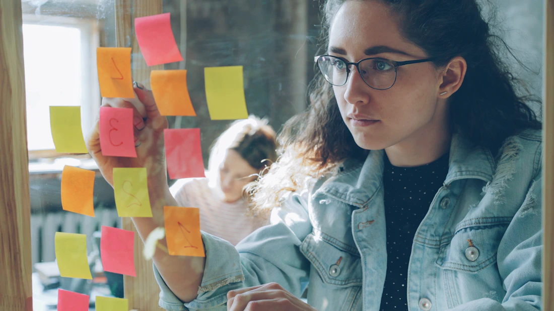Emprendedoras jóvenes organizando ideas mediante notas de colores en una oficina luminosa