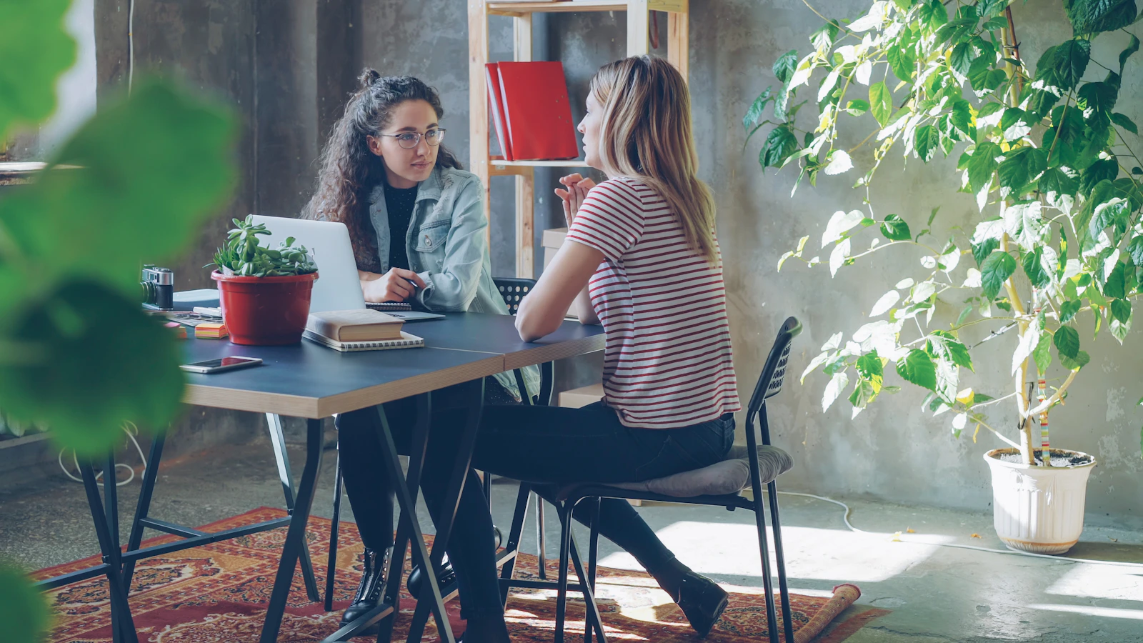 Two professional women sitting at a desk and having a business conversation in a modern office