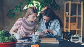 Two women collaborate on a project at a table.