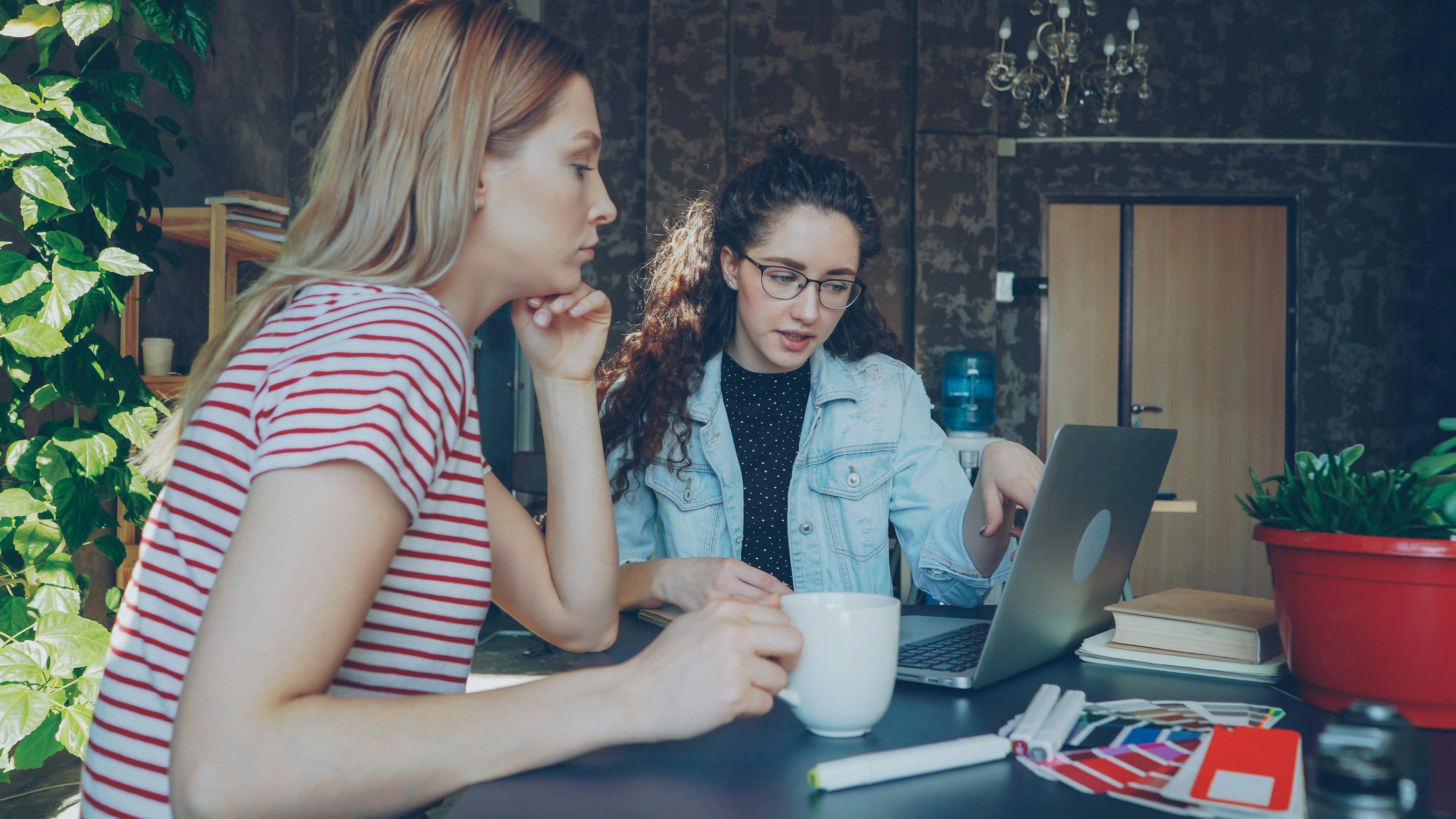 Two women discuss something on a laptop.