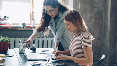 Two women work on a laptop together.