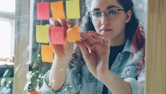 Woman is working with sticky notes on glass.