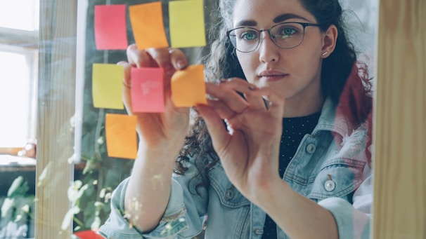 Woman is working with sticky notes on glass.
