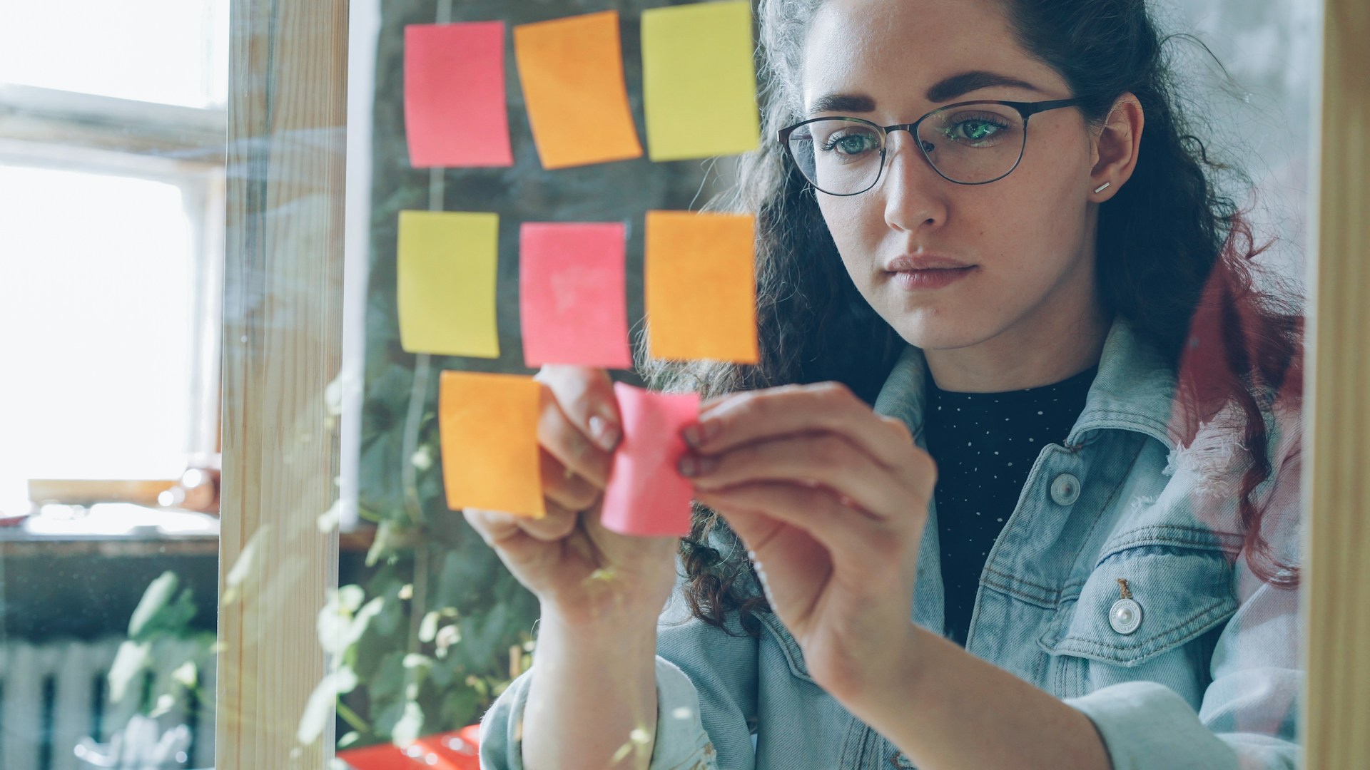 Woman posts sticky notes on a glass wall.