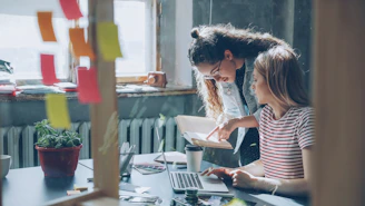 Two women collaborate over a laptop in an office.