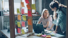 Two women collaborate over a laptop in an office.