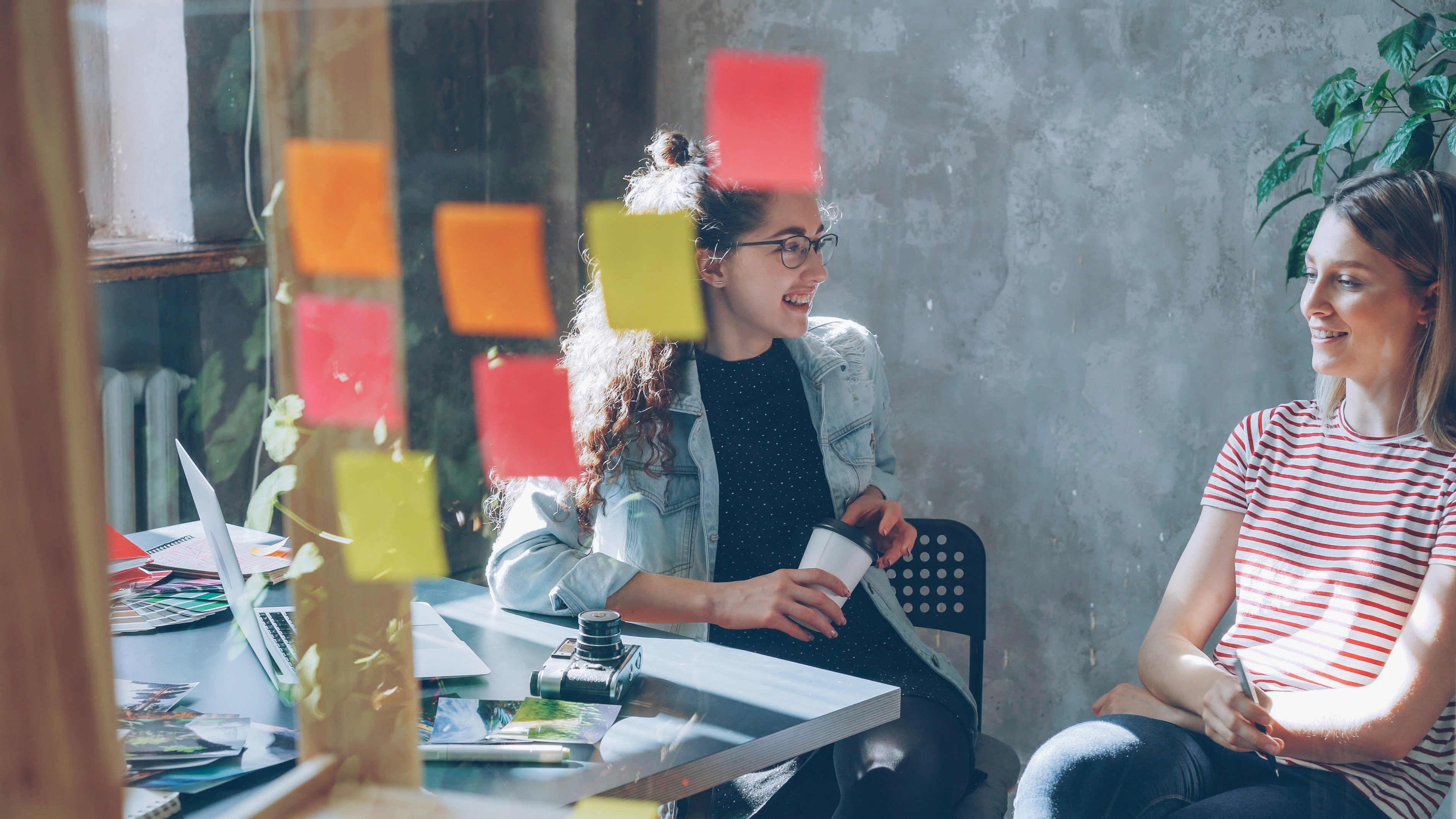 Two women are chatting in a brightly lit office.