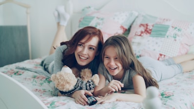 Two girls laugh while relaxing on a bed.