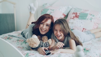Two girls laugh while relaxing on a bed.