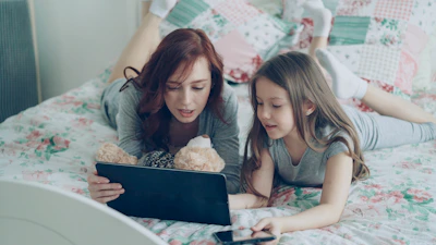 Mother and daughter enjoy a tablet together on bed.