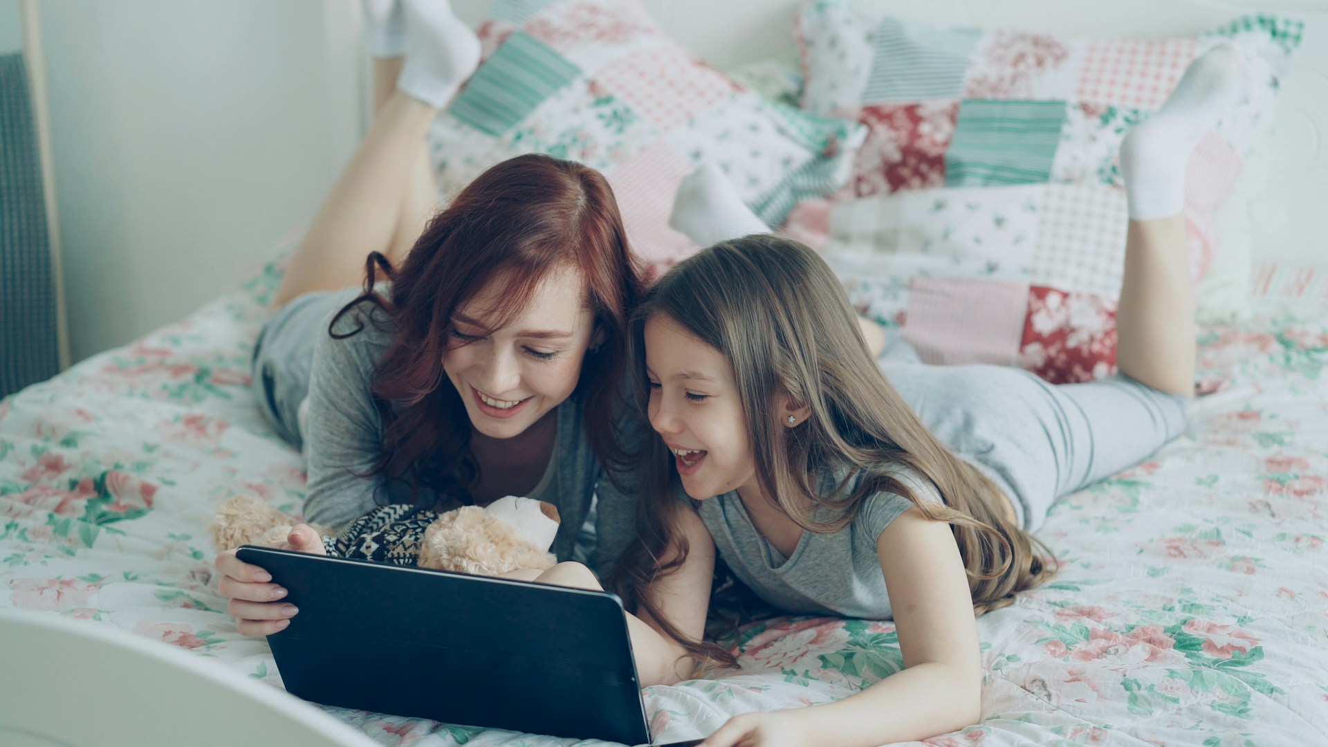 Two girls smile while looking at a tablet.