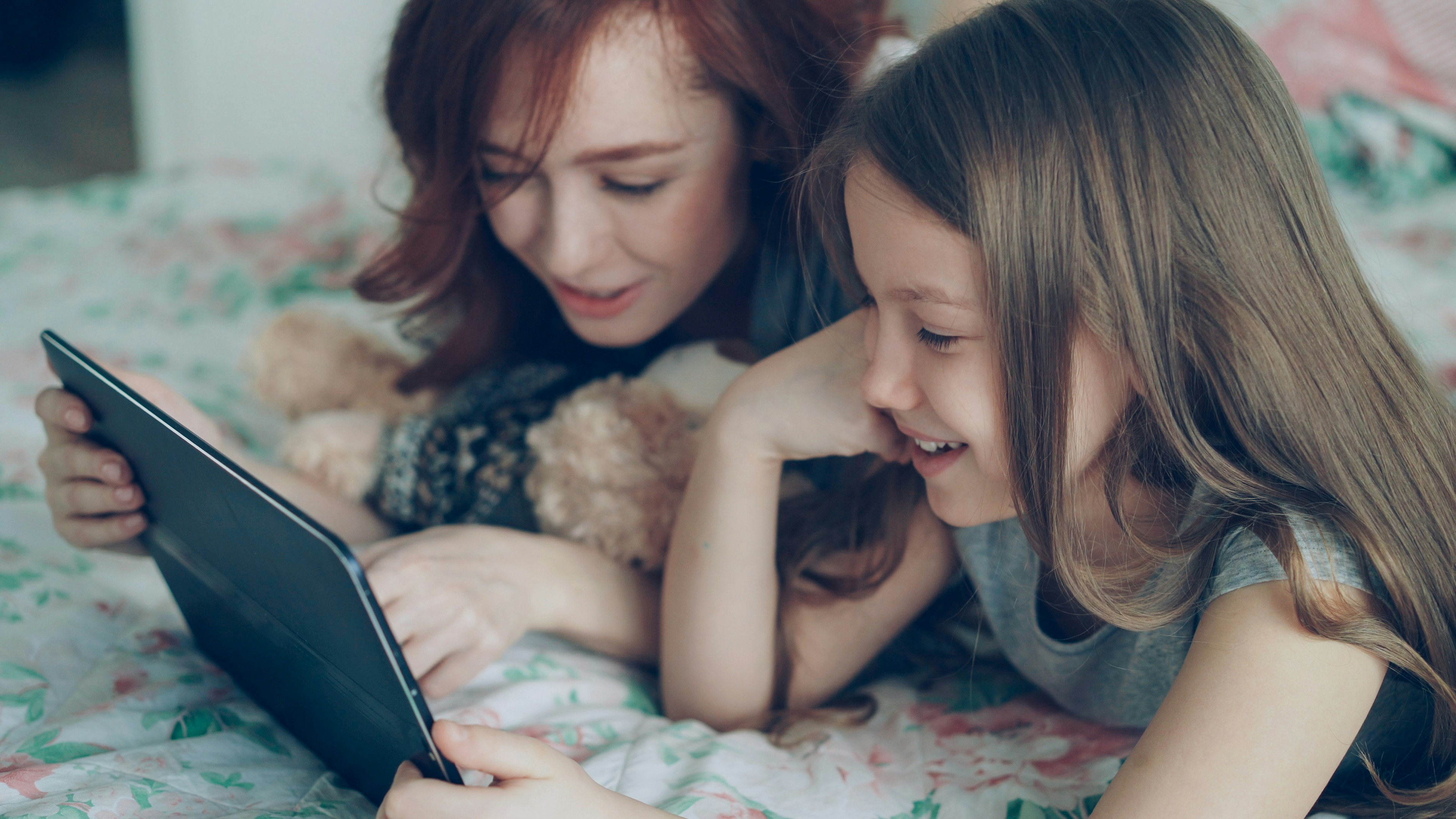 Two girls smile while looking at a tablet.