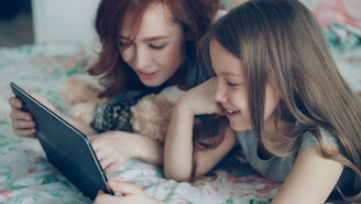 Two girls smile while looking at a tablet